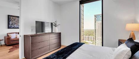 Une chambre moderne avec un grand lit, une commode, un téléviseur et une vue sur la ville.