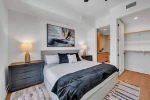 A modern bedroom with a bed, nightstands, a painting, and a walk-in closet.