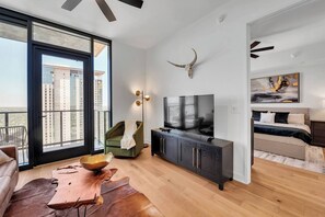 Een moderne woonkamer met een groot raam, een flatscreen televisie, een bank, een salontafel en een plafondventilator.