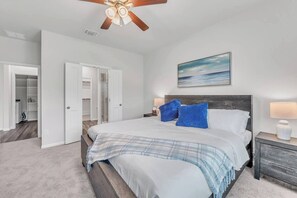 A bedroom with a bed, bedside tables, a ceiling fan, and a painting on the wall.