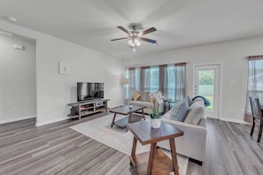 A modern living room with a flat-screen TV, a ceiling fan, a sofa, a coffee table, and a dining table.