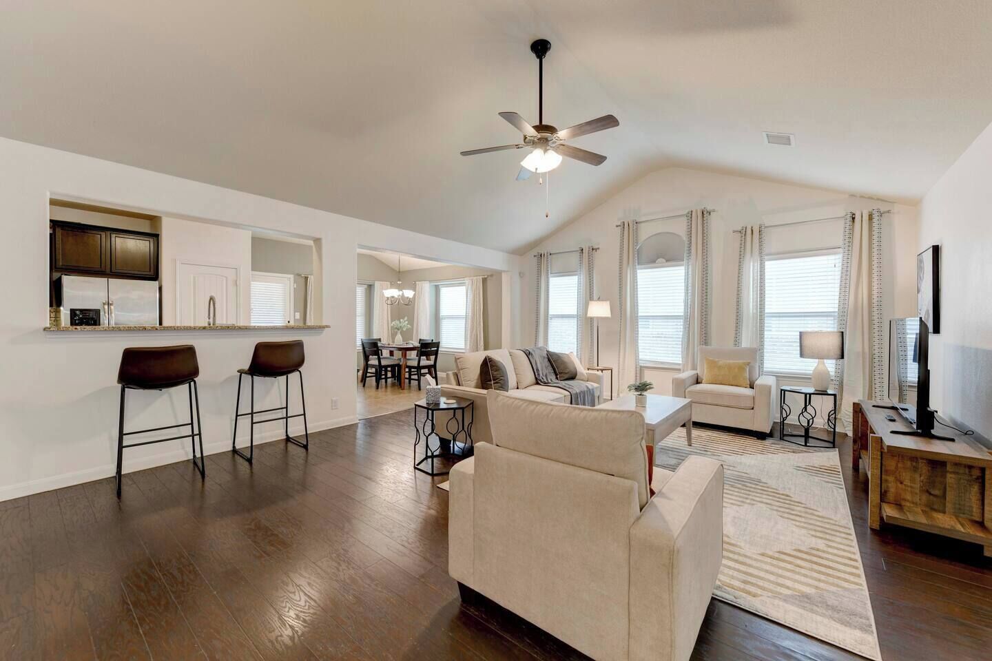 A spacious living room with a large sofa, a dining area, and a kitchen with bar stools.