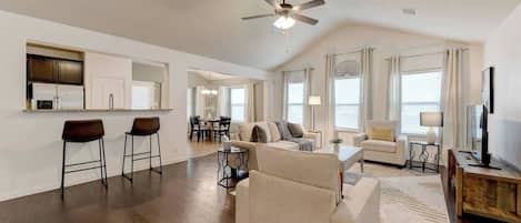 A spacious living room with a large sofa, a dining area, and a kitchen with bar stools.