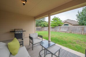 A covered patio area with a grill, a glass table, and a sofa with cushions. - Cedar Park Executive Stay (Cedar Park)