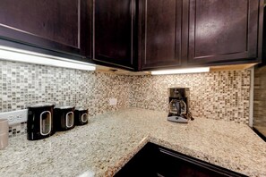 A kitchen with dark cabinets, a tiled backsplash, a granite countertop, and a coffee maker. - Cedar Park Executive Stay (Cedar Park)