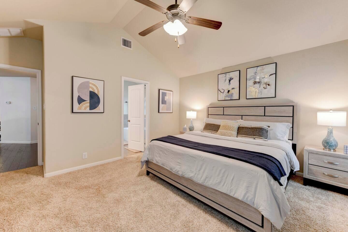 A bedroom with a bed, a nightstand, a ceiling fan, and artwork on the walls.