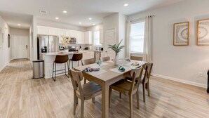 A modern kitchen with white cabinets, a central island, and a dining area with a wooden table and chairs.