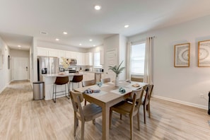 A modern kitchen with white cabinets, a central island, and a dining area with a wooden table and chairs.