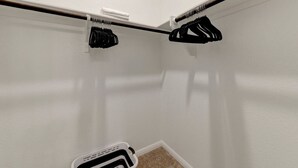 A corner of a room with a white wall, a black coat rack, and a white trash bin.