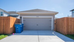 A garage with a number 2438 on the door, a concrete driveway, and two blue recycling bins.