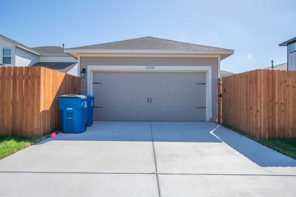 A garage with a number 2438 on the door, a concrete driveway, and two blue recycling bins.