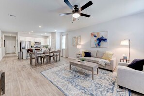 A modern living room with a sofa, coffee table, and a dining area with chairs and a table.