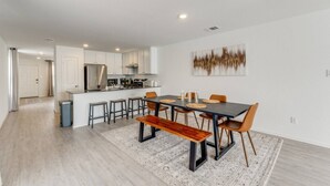 A modern kitchen with white cabinets, a stainless steel range hood, and a dining area with a dark table and wooden chairs.