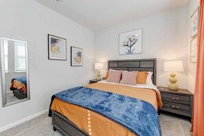 A bedroom with a bed, two bedside tables, a nightstand, a mirror, and framed artwork on the wall. - Round Rock Executive Suite (Round Rock)