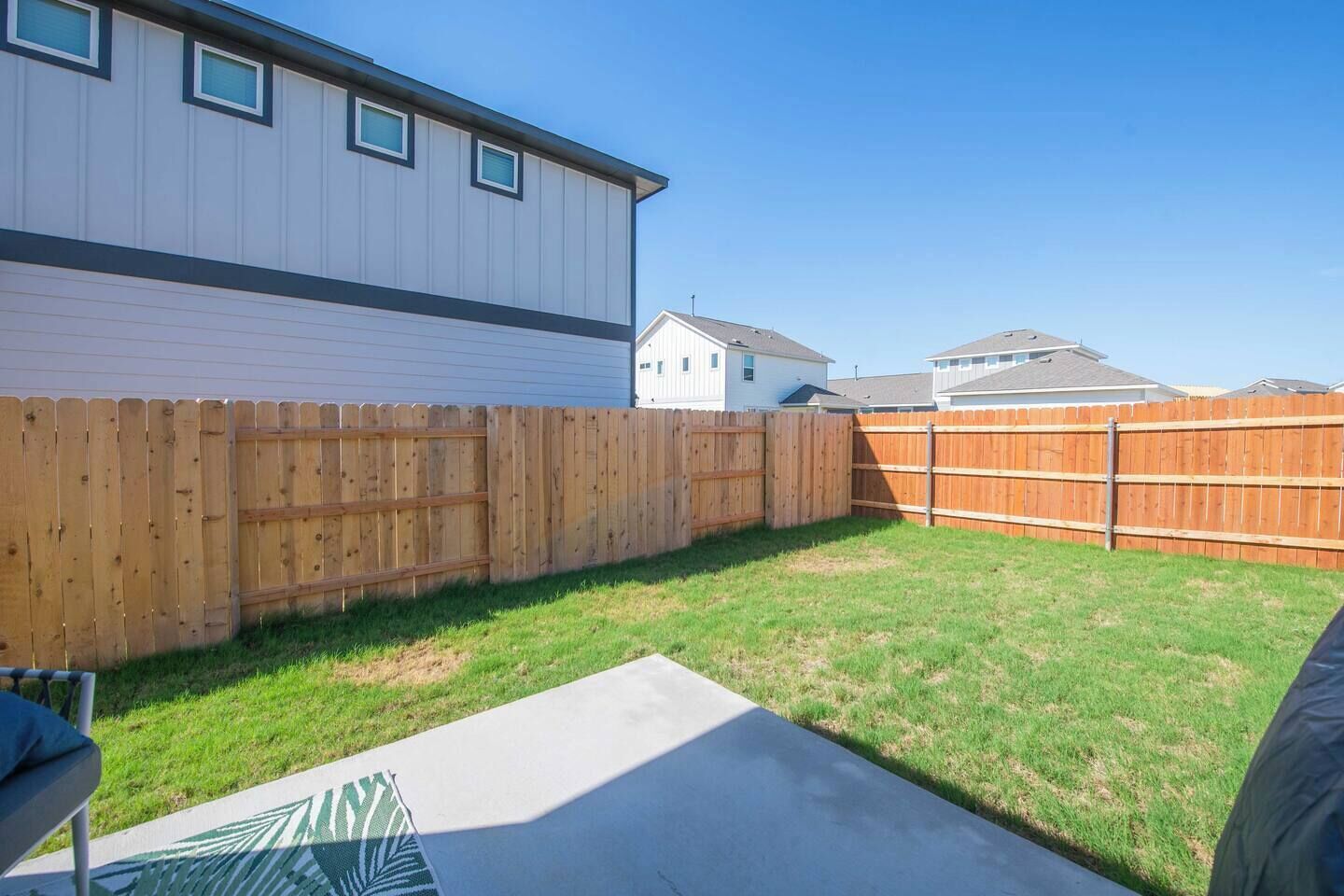 A backyard with a wooden fence, a concrete patio, and a house in the background.