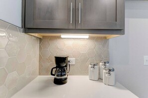 A kitchen with a coffee maker, four condiment containers, and a hexagonal tile backsplash.