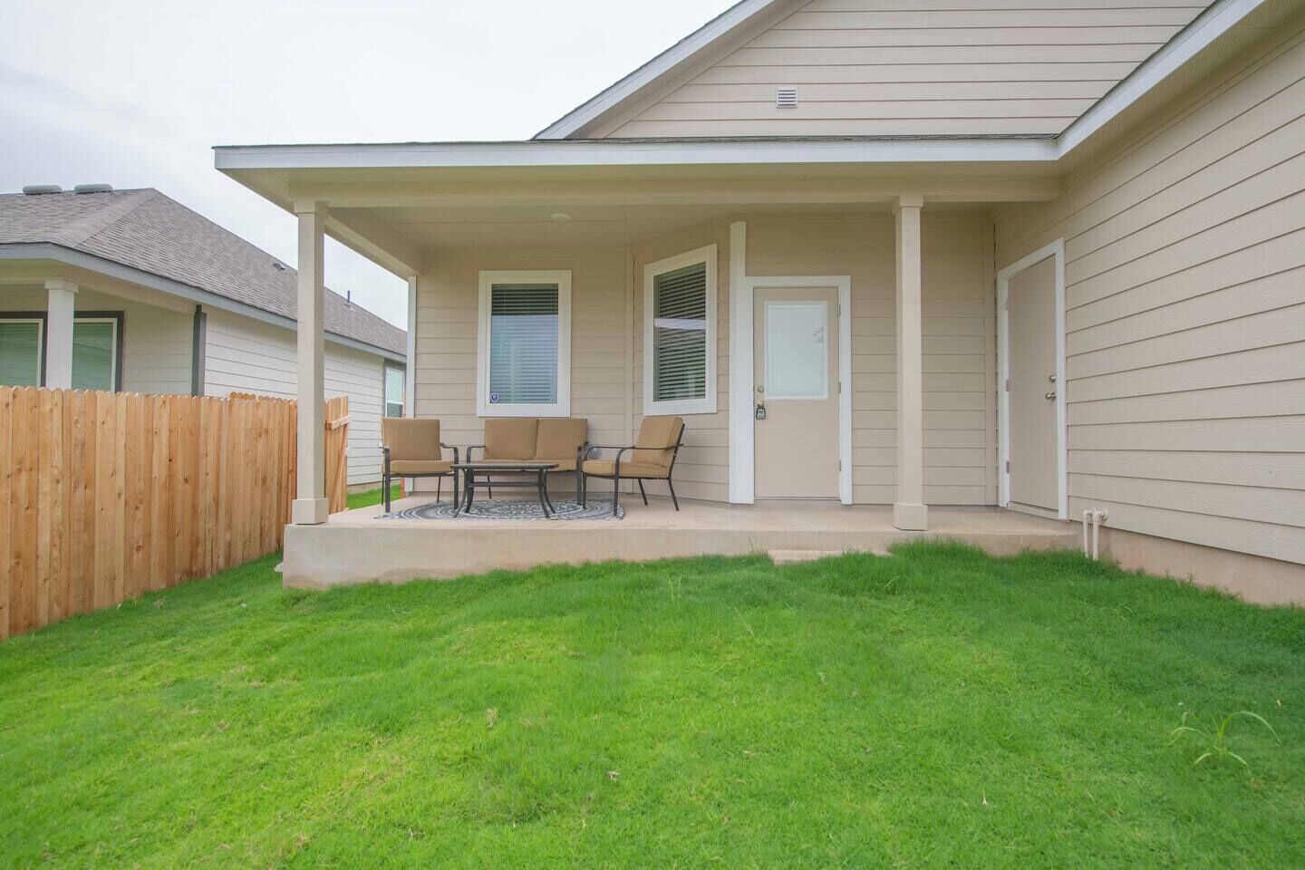 A residential house with a covered patio, a wooden fence, and a well-maintained lawn.