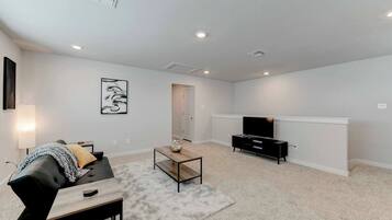 A living room with a sofa, coffee table, TV stand, and artwork on the wall.