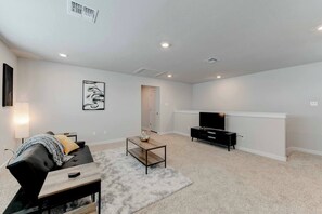 A living room with a sofa, coffee table, TV stand, and artwork on the wall. - Hutto Executive Space (Hutto)