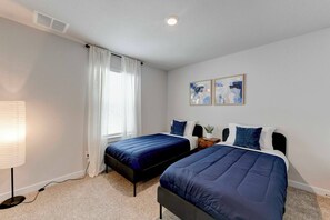 A room with two beds, a lamp, a window with curtains, and two framed pictures on the wall. - Hutto Executive Space (Hutto)