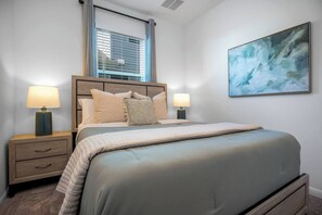 A bedroom with a bed, two bedside tables, a window with blinds, and a painting on the wall.