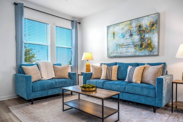 Un salon avec deux canapés bleus, une table basse et un tableau accroché au mur.
