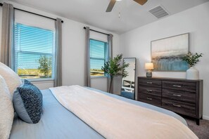 Une chambre à coucher avec un lit, une commode, un miroir et un tableau accroché au mur.