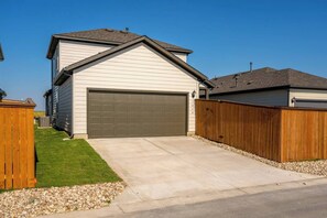 Un garage attenant à une maison, avec une porte sombre, une allée menant au garage et une clôture en bois entourant la propriété.