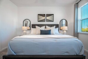 Een slaapkamer met een groot bed, twee spiegels aan de muur en een raam met jaloezieën.