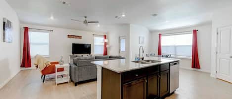 Un apartamento moderno con isla de cocina, sala de estar con sofá y televisor, y comedor con mesa y sillas.
