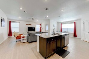 A modern apartment with a kitchen island, a living area with a sofa and TV, and a dining area with a table and chairs. - Brand New 4B Home in Jarrell (Jarrell)