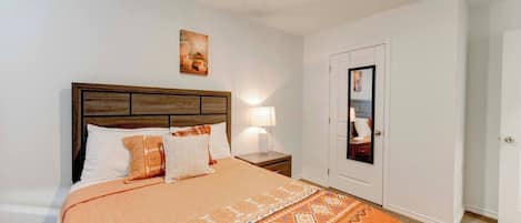A bedroom with a bed, nightstand, lamp, and a door with a mirror.