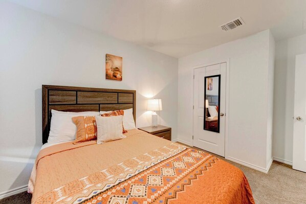 A bedroom with a bed, nightstand, lamp, and a door with a mirror. - Brand New 4B Home in Jarrell (Jarrell)