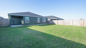 A single-story house with a covered patio, a fenced backyard, and a clear sky.