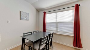 A dining area with a table and chairs, a window with blinds, and a red curtain.