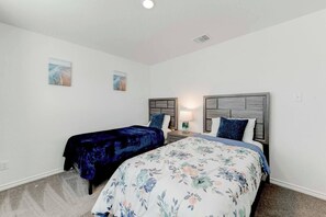 A bedroom with two beds, a nightstand with a lamp, and two wall-mounted artworks. - Brand New 4B Home in Jarrell (Jarrell)