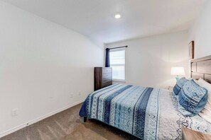 A bedroom with a bed, a dresser, a nightstand, and a window with blinds.