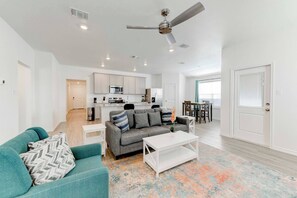 A modern apartment with a living room, kitchen, dining area, and a ceiling fan.