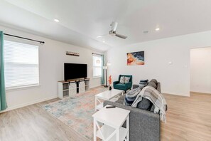 A modern living room with a flat-screen TV, a green armchair, a gray sofa, and a colorful rug.