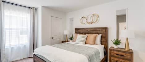 A bedroom with a wooden bed, a nightstand, a mirror, and a window with curtains.