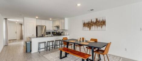 A modern kitchen with white cabinets, a stainless steel range hood, and a dining area with a dark table and wooden chairs.