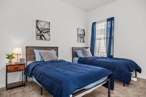 A bedroom with two beds, a nightstand with a lamp, and artwork on the walls.