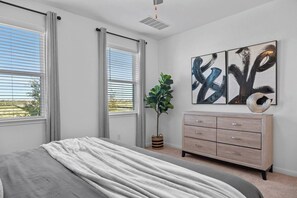 A bedroom with a bed, a dresser, a potted plant, and abstract art on the wall.