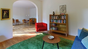 A living room with a red armchair, a bookshelf, a round coffee table, and a green rug.