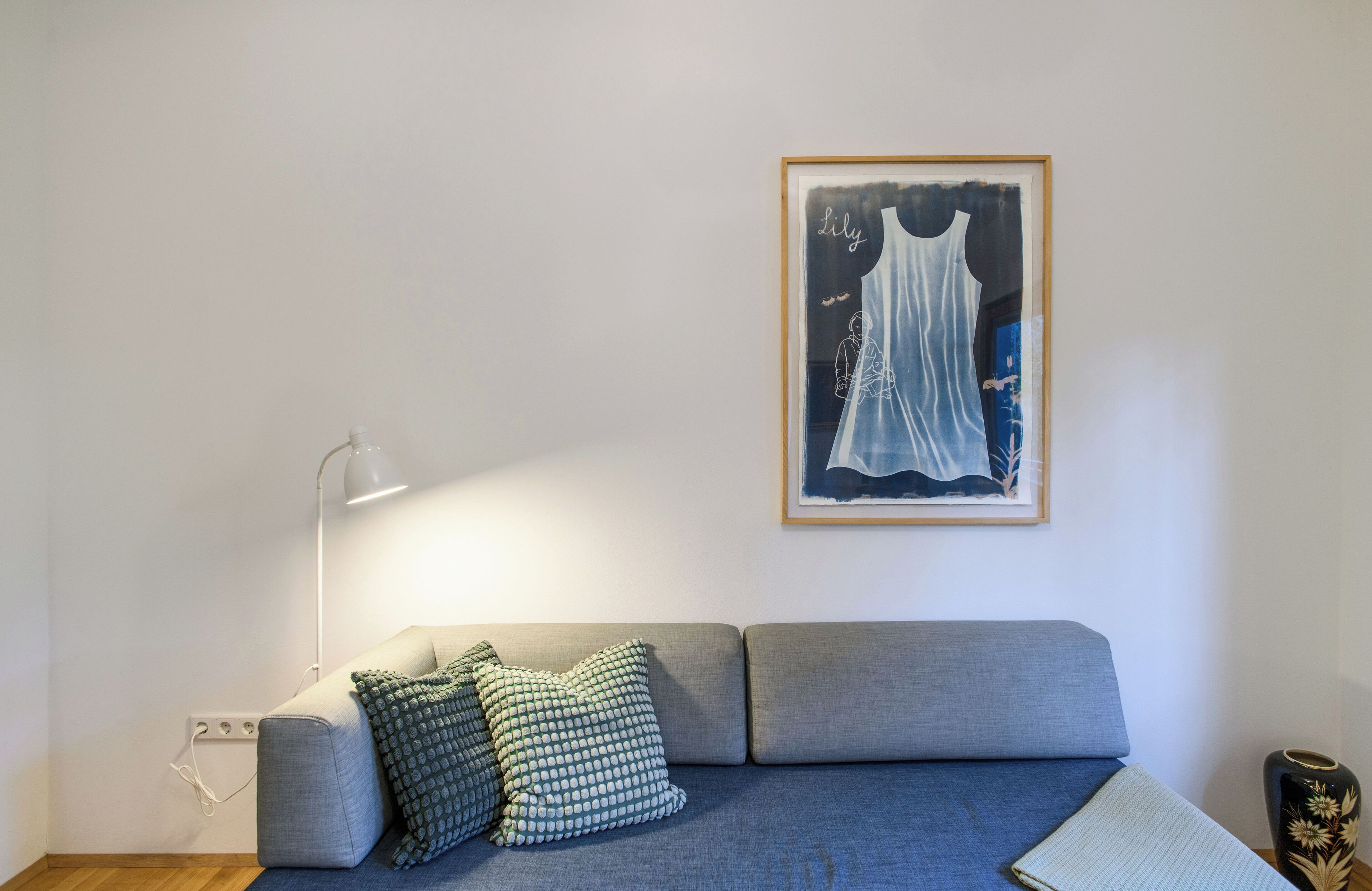 A modern living room with a grey sofa, patterned pillows, a framed artwork, a floor lamp, and a vase.