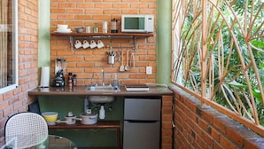 A compact kitchen with a brick wall, a microwave, and various utensils on a shelf. - Casa Redonda 🌼 Casita 1 🌞SayulitaWifi 💛 Central (Sayulita)