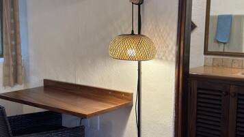 Um quarto com uma mesa de madeira, cadeira de vime e um candeeiro suspenso.