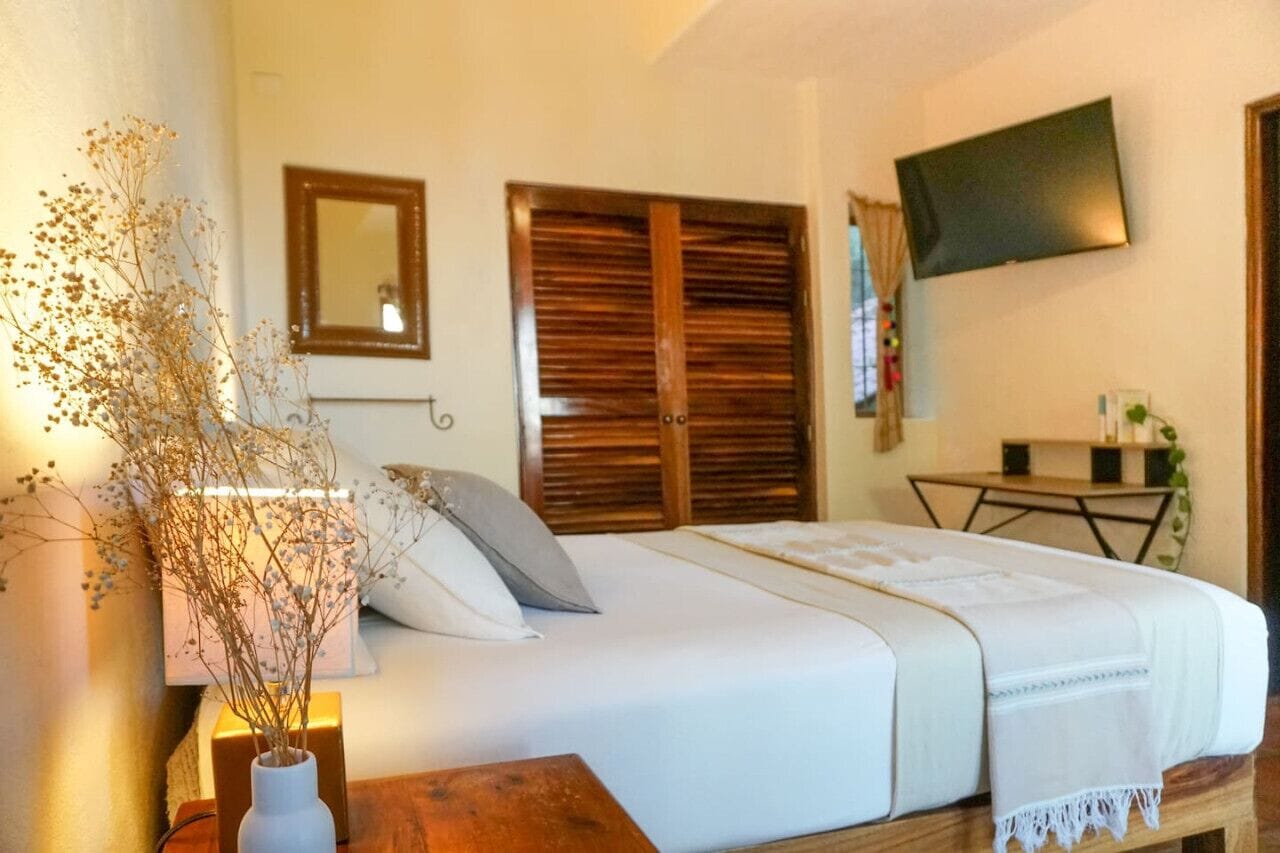 Une chambre à coucher comprenant un lit, une table de chevet, un miroir, une télévision et une armoire en bois.