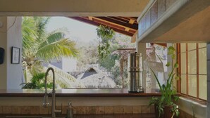Una cocina con un ventanal grande que da a un jardín, un lavamanos y una planta en maceta.