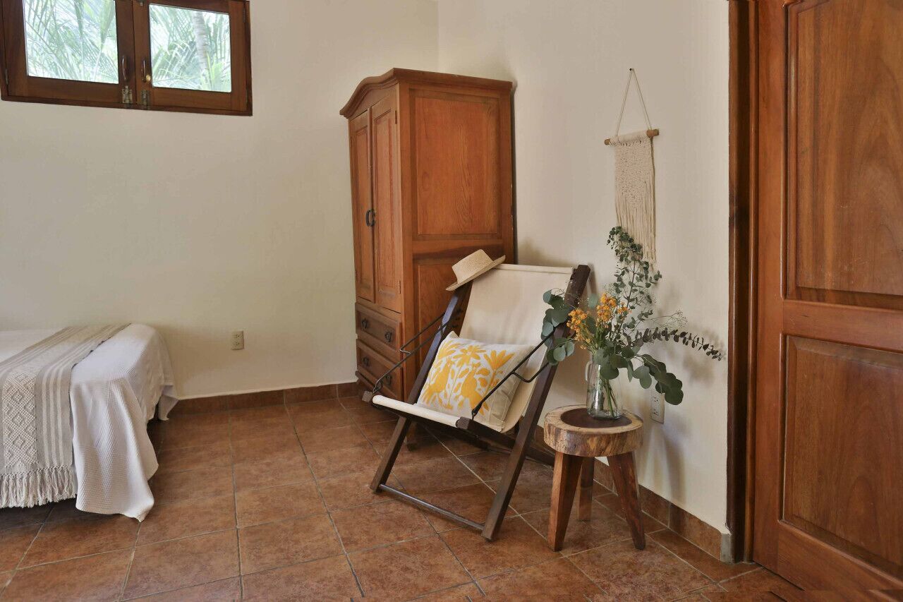 Een kamer met een bed, een houten garderobe, een houten stoel en een kleine tafel met een plant.